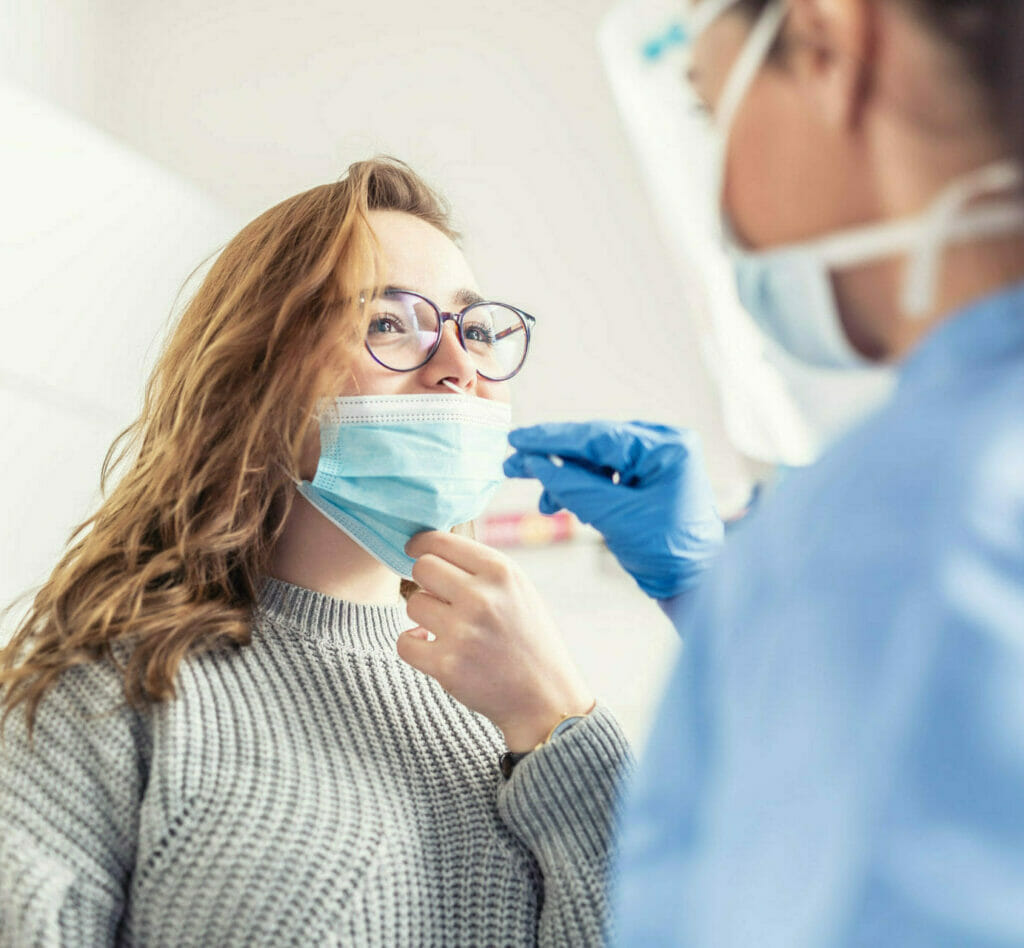 Image of medical professional administering a covid test to girl, while she lowers the mask off her nose.